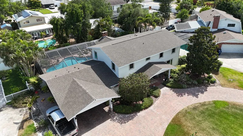 Aerial view of a completed architectural shingle roof on a two-story Southwest Florida home with a screened pool enclosure and paver driveway