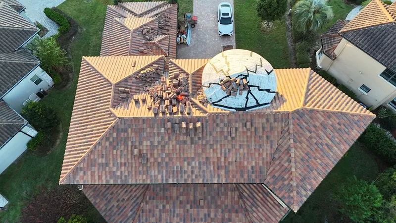 Aerial view of a barrel-tile roof repair in evening light, with tiles lifted around a circular turret and the sealed underlayment exposed beneath