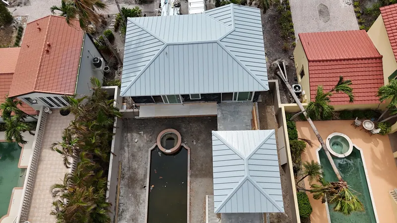Aerial view of a newly installed light-gray standing-seam metal roof on a coastal Southwest Florida property between neighboring tile-roofed homes