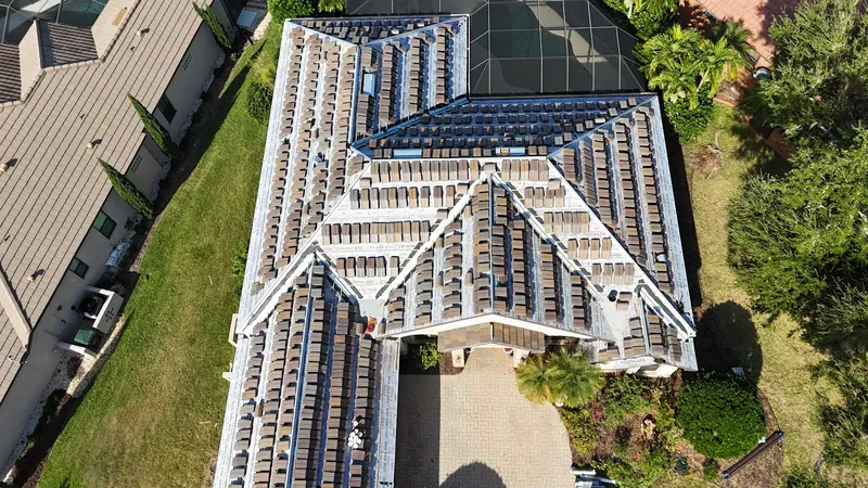 Overhead view of a tile roof installation in progress, with new tiles staged in rows across fresh Polyglass underlayment beside a screened pool cage